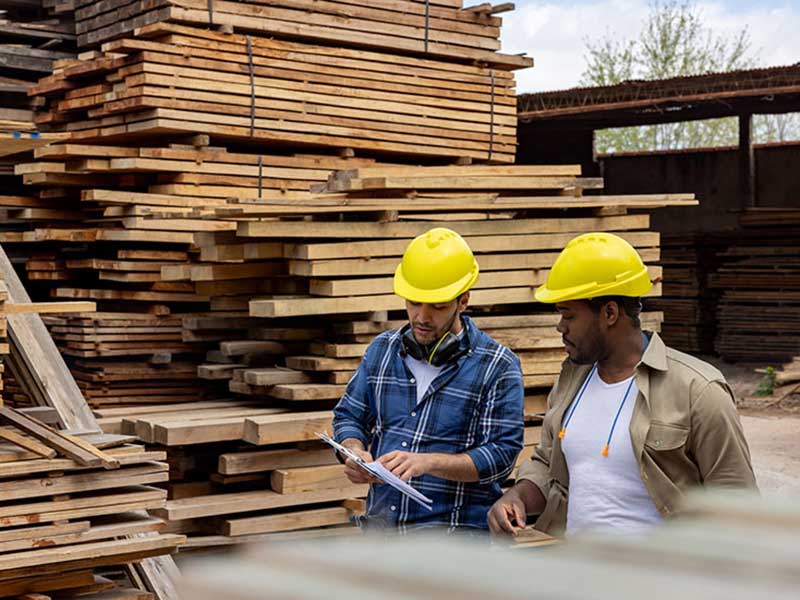 workers talking near stacks wood boards in local lumber yard